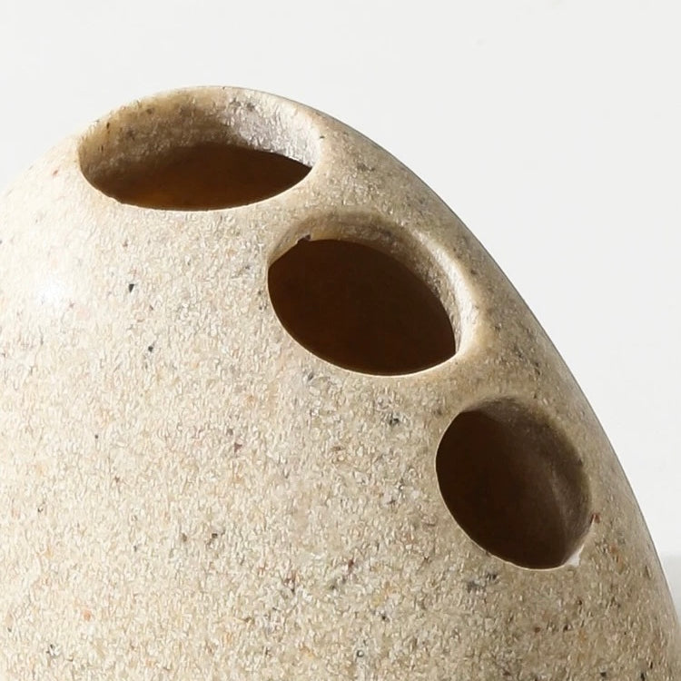Close-up of a beige ceramic vase with three circular holes on a light gray background