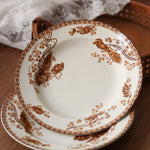 Set of white plates with brown floral patterns on a wooden surface.