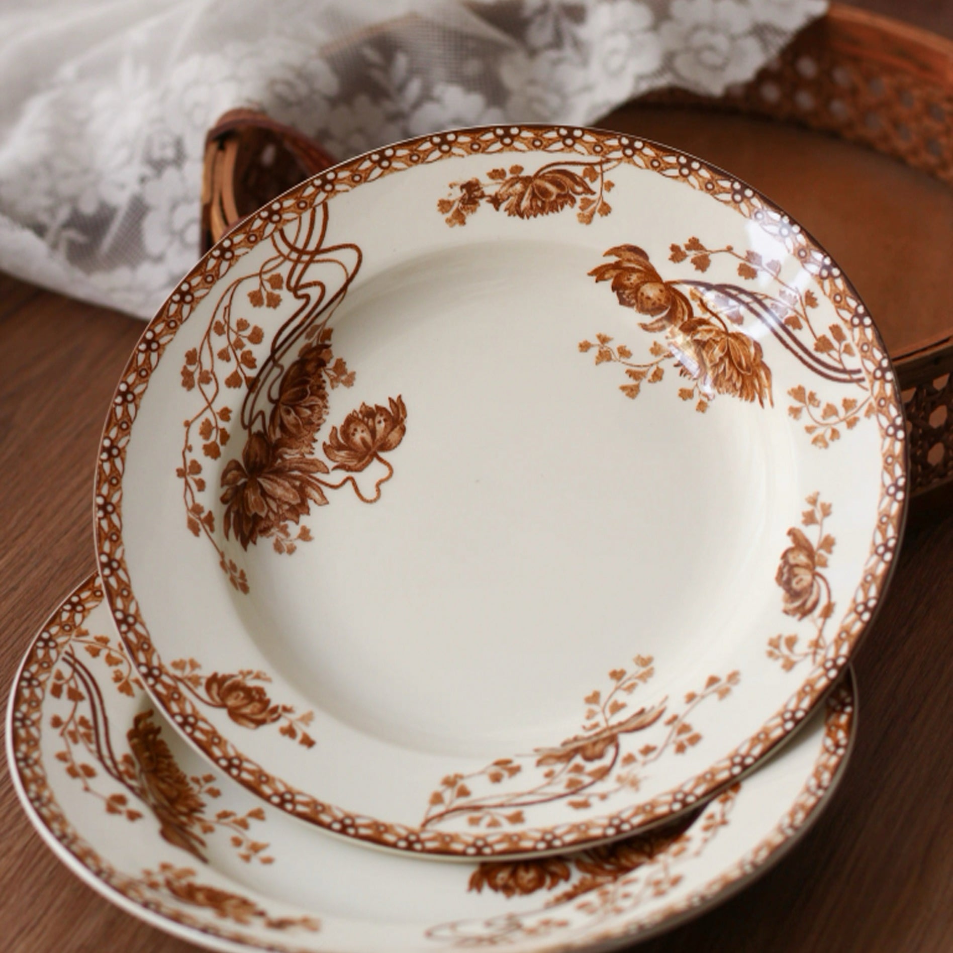 Set of white plates with brown floral patterns on a wooden surface.