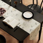 Table setting with a patterned table runner, open book, and fruit on a black table.