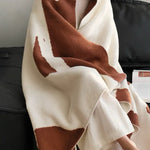 Person wrapped in a brown and white patterned blanket sitting on a couch.