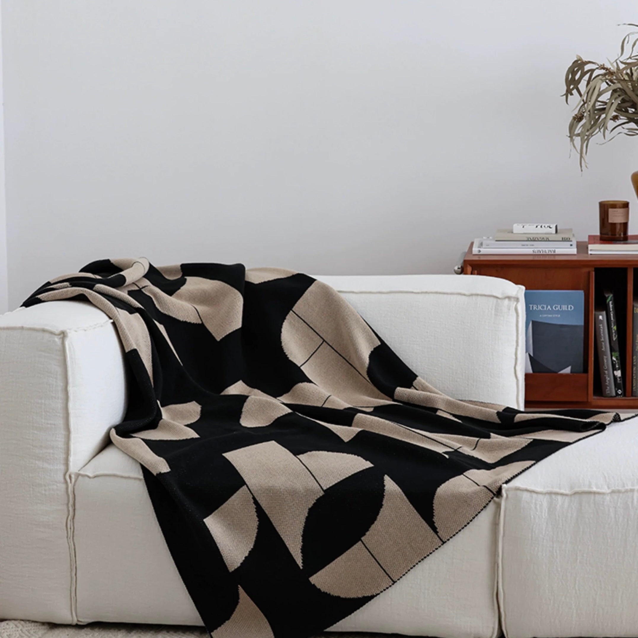 Black and beige patterned blanket draped over a white sofa in a living room setting.