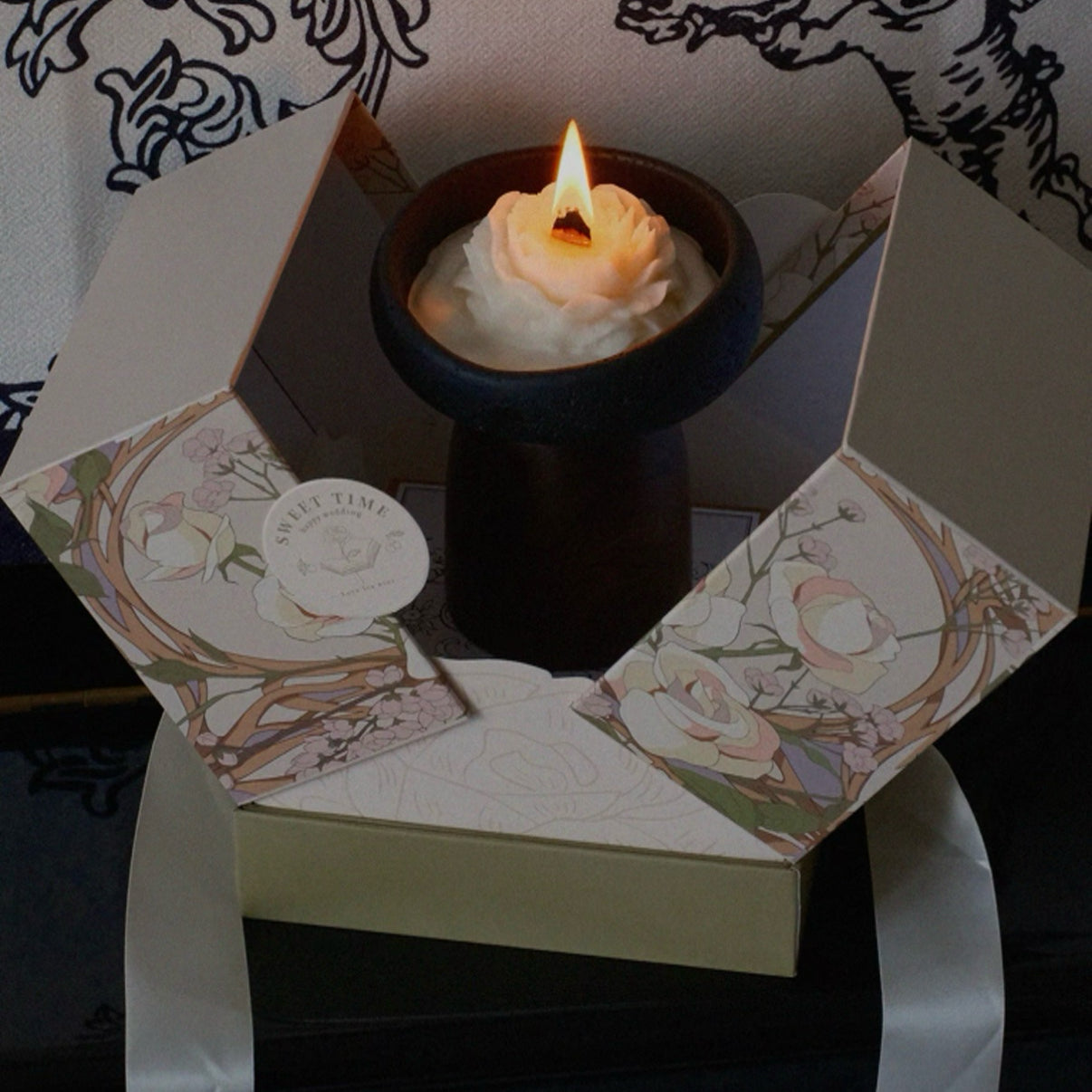 Candle in a decorative box with floral design on a dark background