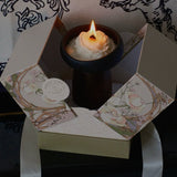 Candle in a decorative box with floral design on a dark background