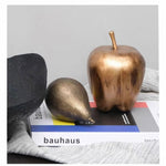 Decorative objects including a bronze apple and pear on a 'Bauhaus' book with a gray background