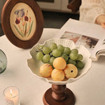 Decorative fruit bowl with grapes and pears on a wooden stand, candle, and book in the background.