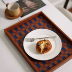 Wooden checkered tray with a plate of food and a cup on a white surface.