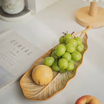 Leaf-shaped ceramic plate with grapes and a peach on a white surface.