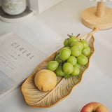 Leaf-shaped ceramic plate with grapes and a peach on a white surface.