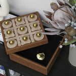 Wooden tic-tac-toe game set with gold pieces on a dark surface.