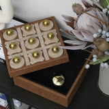 Wooden tic-tac-toe game set with gold pieces on a dark surface.