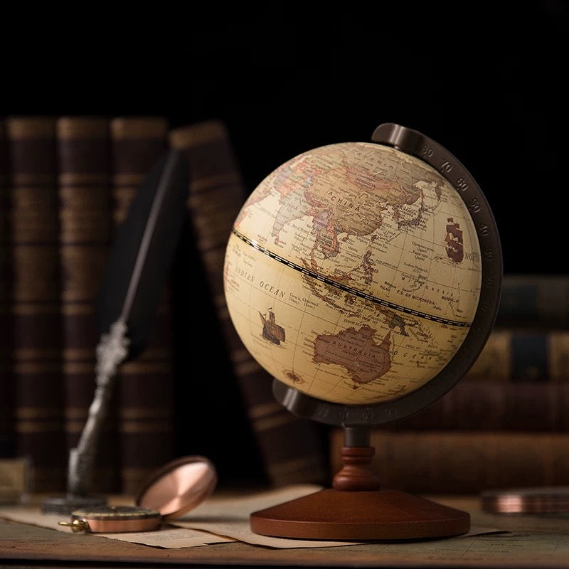 Vintage-style world globe on a wooden stand with books and quill in the background