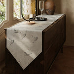 Table runner with feather design on a wooden table near a window