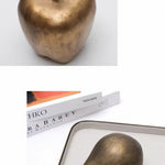 Bronze apple and pear on a white surface with books in the background