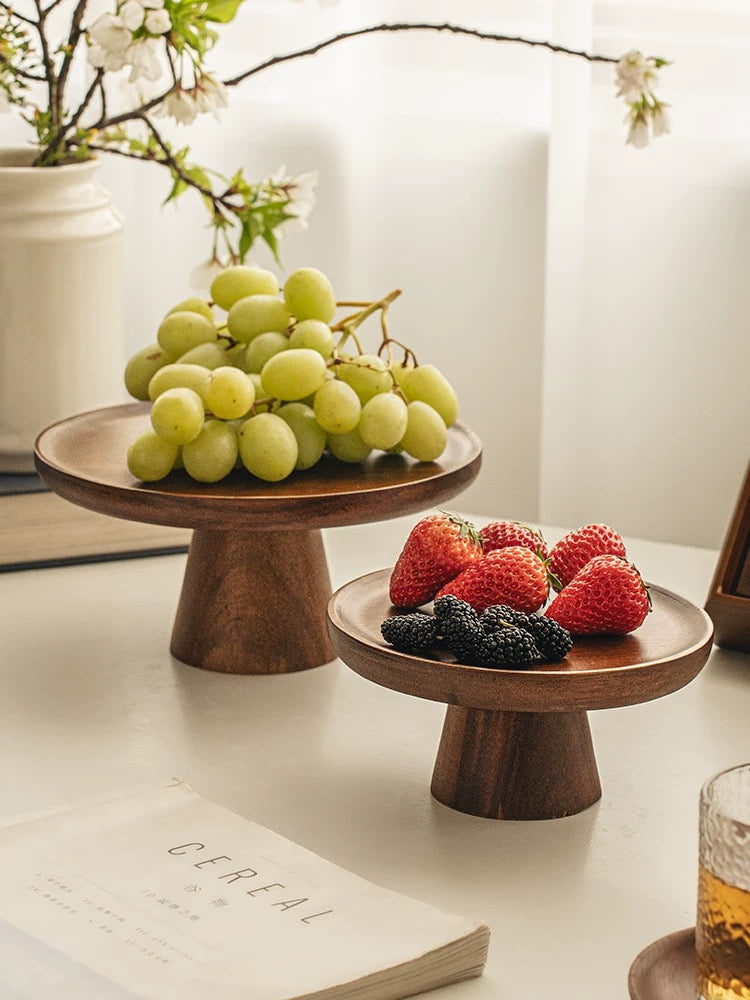 Wooden fruit stands with grapes and berries on a table with a book and glass in the background.