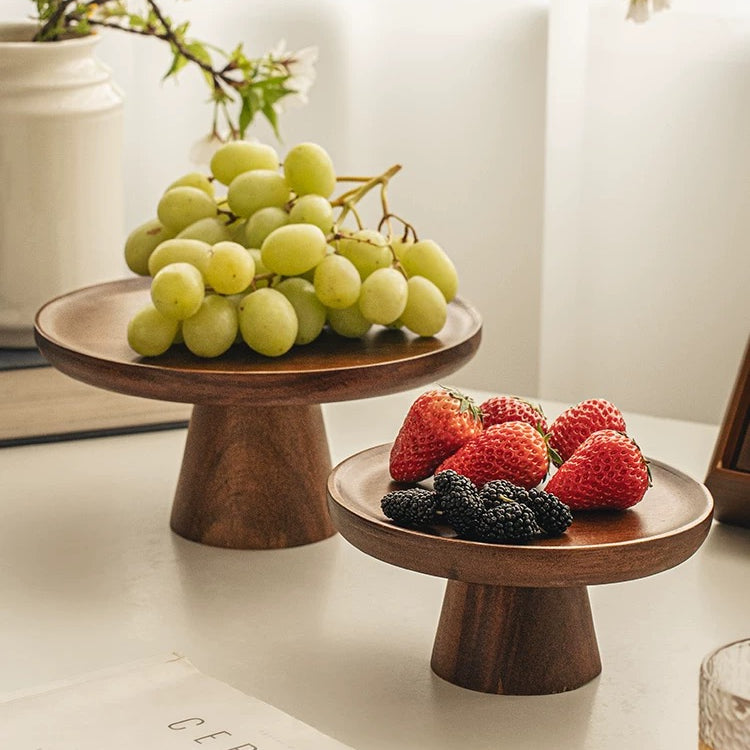 Wooden fruit stands with grapes and berries on a table with a book and glass in the background.