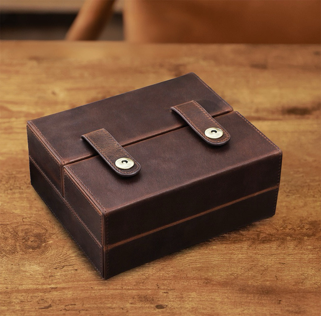 Brown leather box with two straps on a wooden surface