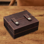 Brown leather box with two straps on a wooden surface
