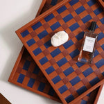 Two wooden trays with a checkered pattern, one with a bottle and a bar of soap on a white surface.