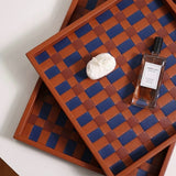 Two wooden trays with a checkered pattern, one with a bottle and a bar of soap on a white surface.