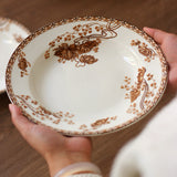 Person holding a decorative ceramic plate with brown floral patterns on a wooden surface