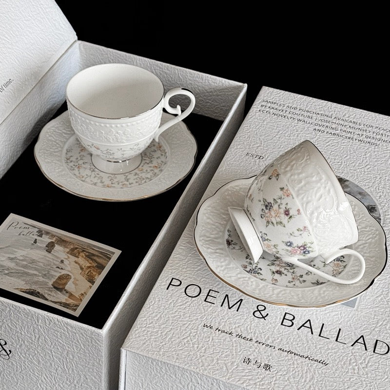 White ceramic cup and saucer set on a box labeled 'POEM & BALLAD' with a black background.