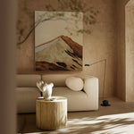 Modern living room with a beige sofa, wooden side table, and abstract mountain painting.