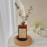 A bottle of 'Floral Petals' diffuser with flowers on a wooden stand on a white surface.