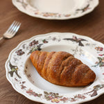 Croissant on a decorative plate with a floral pattern on a wooden table.