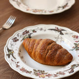 Croissant on a decorative plate with a floral pattern on a wooden table.