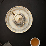 Decorative teapot on a black surface with a cup of tea nearby