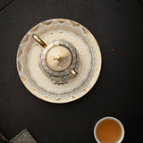 Decorative teapot on a black surface with a cup of tea nearby