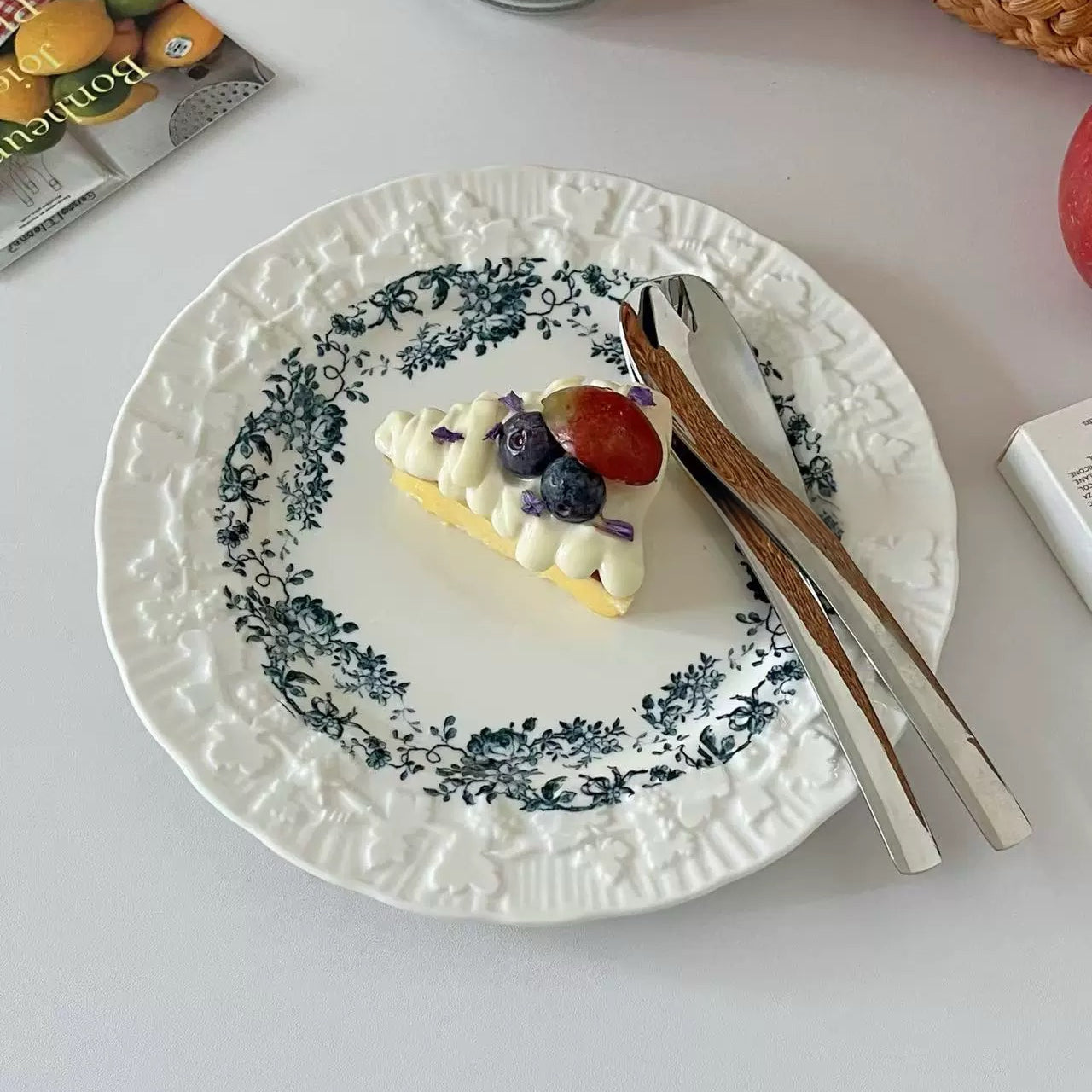 Small dessert with berries on a decorative plate with cutlery, on a light surface.