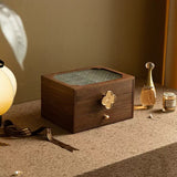 Wooden jewelry box with a gold handle on a textured surface with decorative items.