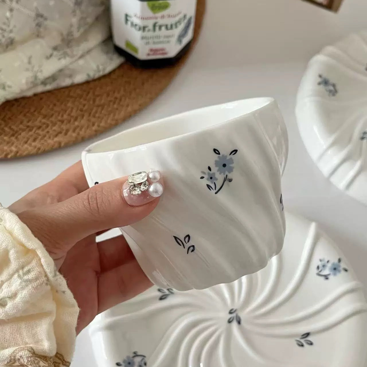 Hand holding a white ceramic pot with floral designs on a blurred background