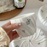 Hand holding a white ceramic pot with floral designs on a blurred background