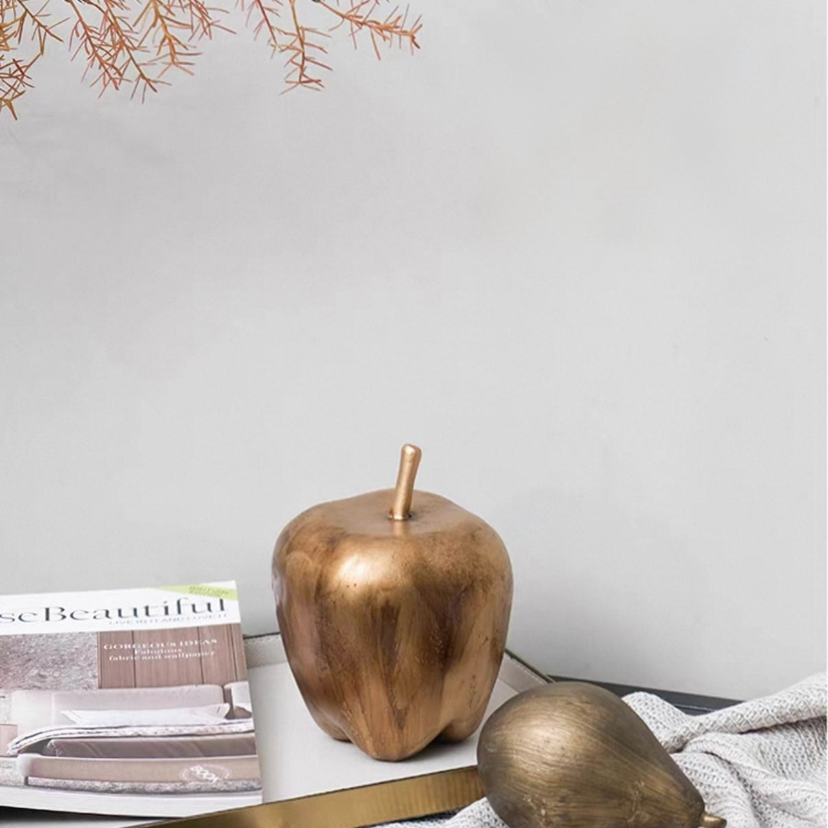 Bronze apple and pear on a table with a magazine and branch in the background