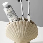 Shell-shaped holder with toothbrushes and toothpaste on a gray background