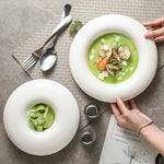 Two white bowls with green soup and seafood on a textured surface with cutlery.