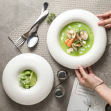 Two white bowls with green soup and seafood on a textured surface with cutlery.