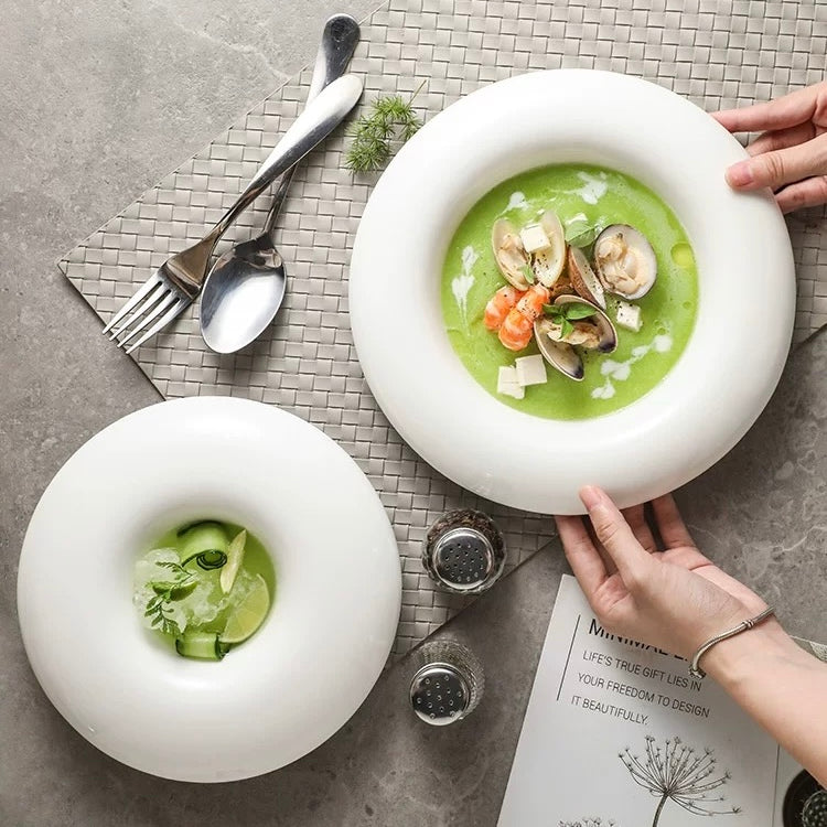 Two white bowls with green soup and seafood on a textured surface with cutlery.