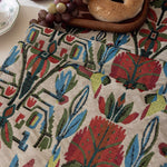 Close-up of a patterned fabric with colorful leaves and flowers on a neutral background.