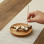 Hand placing an incense stick on a wooden coaster with floral design