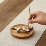 Hand placing an incense stick on a wooden coaster with floral design