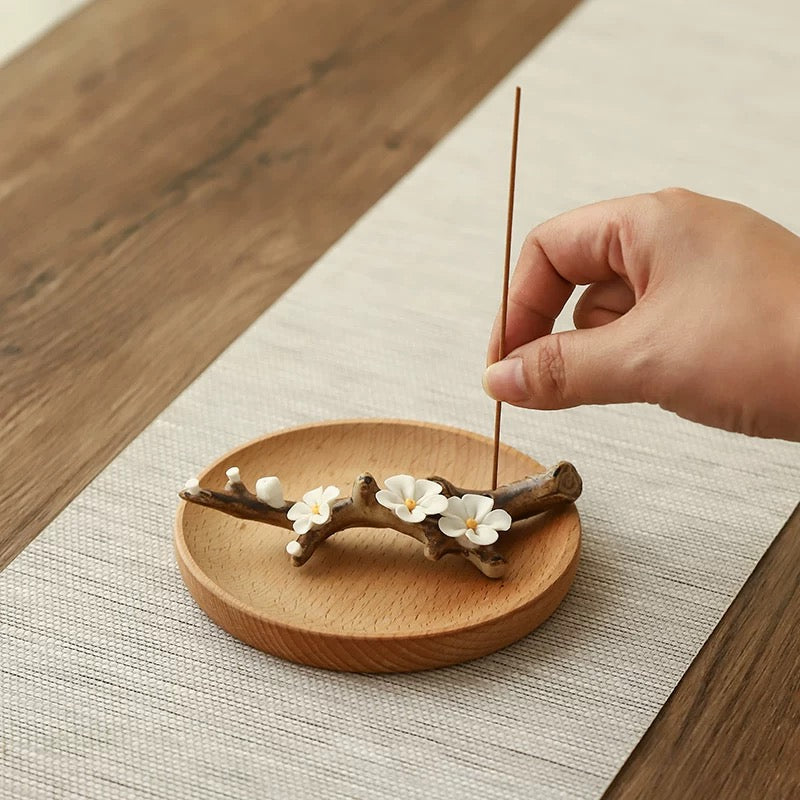 Hand placing an incense stick on a wooden coaster with floral design