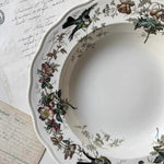 Decorative plate with floral and bird patterns on a surface with handwritten text.