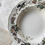 Decorative plate with floral and bird patterns on a surface with handwritten text.