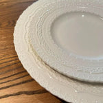 Stack of white ceramic plates with textured rim on a wooden surface