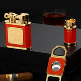 Red and gold lighter, bottle opener, and cigar on a dark surface with a glass of whiskey in the background.