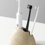 Ceramic toothbrush holder with three toothbrushes on a light gray background